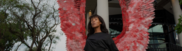 a woman in front of a statue with red wings